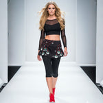 Load image into Gallery viewer, Model walking on a runway wearing a black outfit with a patterned skirt.
