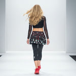 Load image into Gallery viewer, Model walking on a runway wearing a black crop top, patterned skirt, and black leggings with red shoes.
